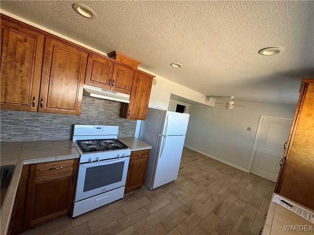 kitchen featuring white appliances, tasteful backsplash, brown cabinets, light countertops, and under cabinet range hood