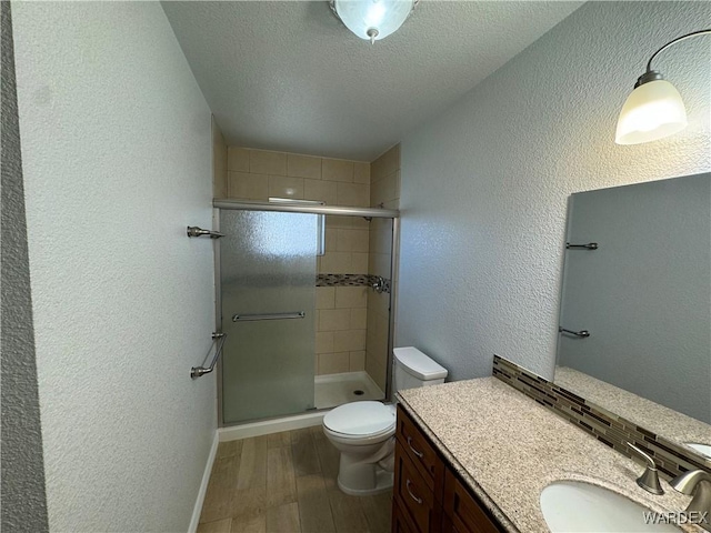 bathroom featuring a textured wall, toilet, a stall shower, a textured ceiling, and wood finished floors