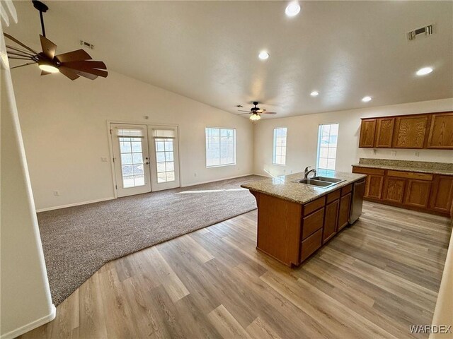 kitchen featuring visible vents, brown cabinets, open floor plan, a kitchen island with sink, and a sink