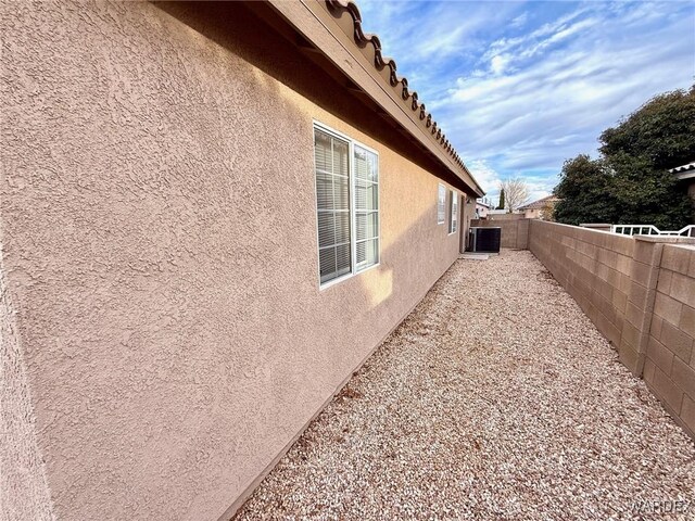 view of side of home featuring a fenced backyard, central AC unit, and stucco siding