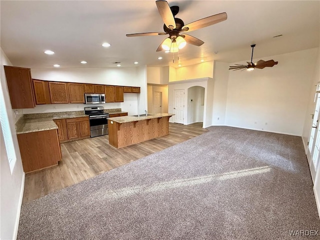 kitchen with light carpet, a kitchen island, open floor plan, appliances with stainless steel finishes, and brown cabinets