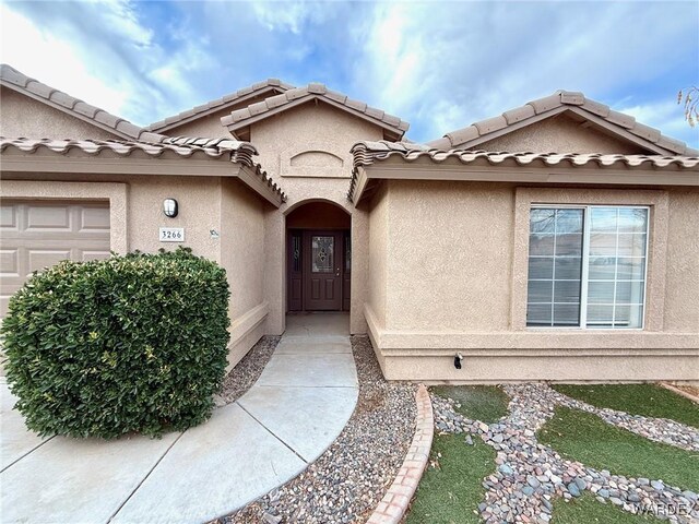 property entrance with a garage, a tiled roof, and stucco siding