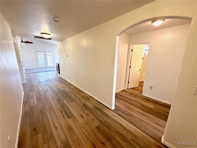 corridor with arched walkways, wood finished floors, and baseboards