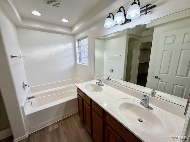 bathroom with a walk in closet, visible vents, a sink, and wood finished floors