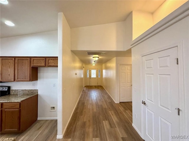 hallway featuring visible vents, a towering ceiling, baseboards, and wood finished floors