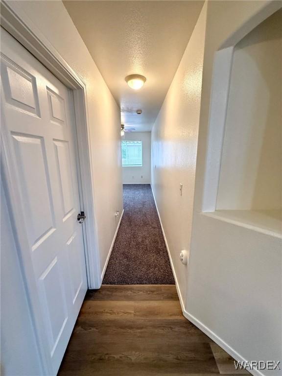 corridor featuring a textured ceiling, baseboards, and dark wood-type flooring