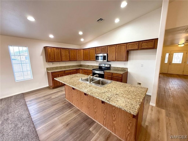 kitchen featuring visible vents, appliances with stainless steel finishes, brown cabinetry, a sink, and light stone countertops