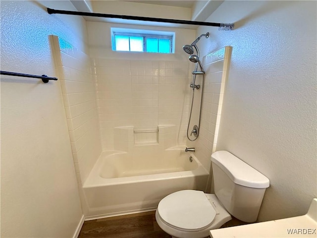 bathroom with a textured wall, bathtub / shower combination, wood finished floors, and toilet