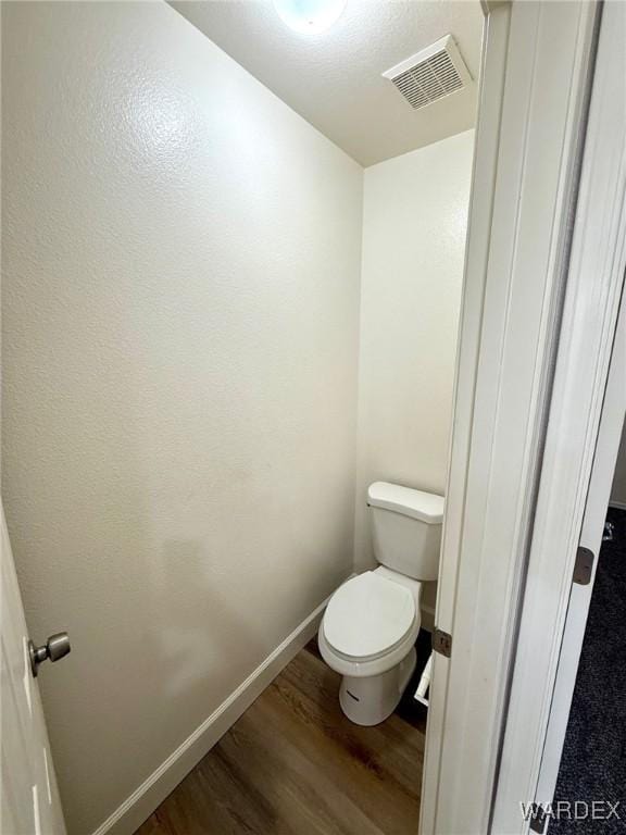 bathroom featuring toilet, wood finished floors, visible vents, and baseboards