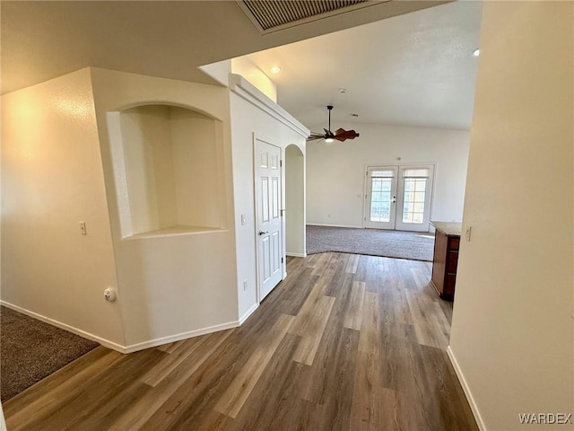 hall featuring arched walkways, wood finished floors, visible vents, and baseboards