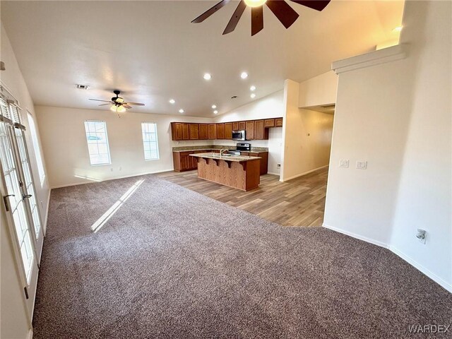 kitchen featuring a center island, brown cabinets, light countertops, open floor plan, and light carpet