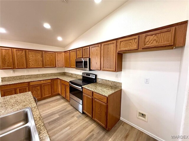 kitchen with brown cabinets, stainless steel appliances, lofted ceiling, light wood-style flooring, and a sink