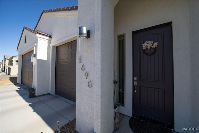 entrance to property with a garage, driveway, and stucco siding