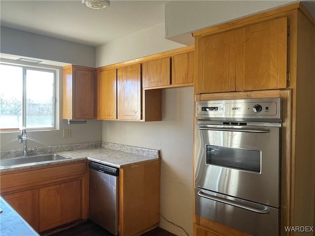 kitchen featuring stainless steel appliances, brown cabinetry, light countertops, and a sink