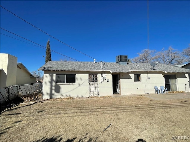 back of property featuring central AC, roof with shingles, concrete block siding, and fence