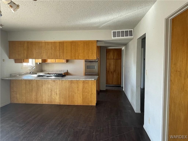 kitchen with a peninsula, visible vents, light countertops, and dark wood-type flooring