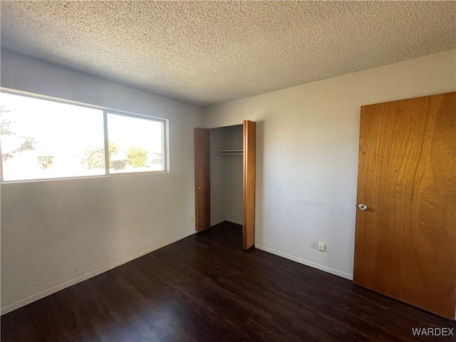 unfurnished bedroom with dark wood-style floors, a closet, a textured ceiling, and baseboards