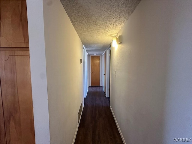 hallway featuring dark wood-style floors, visible vents, baseboards, and a textured ceiling