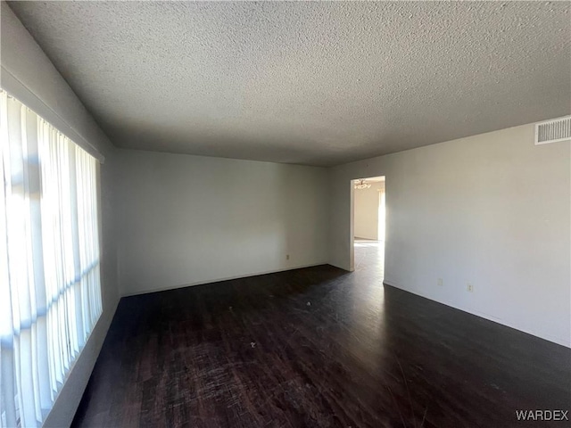 empty room with a textured ceiling, visible vents, and dark wood-style flooring