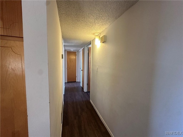 hallway with dark wood-style floors, baseboards, and a textured ceiling