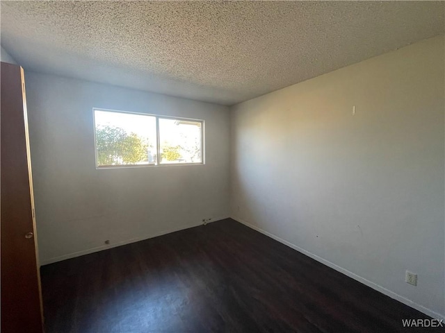 spare room featuring dark wood-style flooring, a textured ceiling, and baseboards