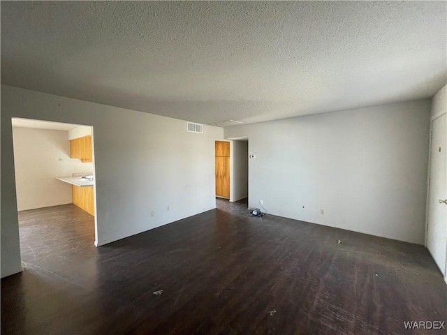 empty room with a textured ceiling, dark wood finished floors, and visible vents