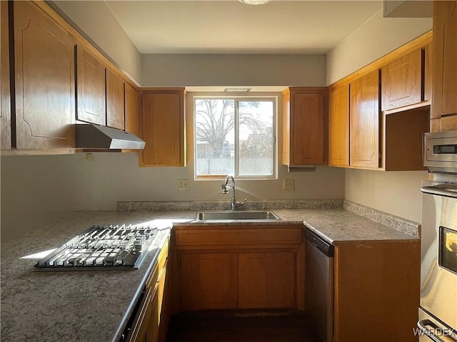 kitchen with dark stone counters, brown cabinets, stainless steel appliances, under cabinet range hood, and a sink