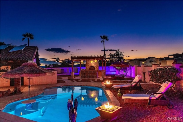 pool at dusk featuring a fenced backyard, exterior fireplace, and a patio