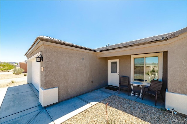 rear view of property featuring a patio, an attached garage, and stucco siding