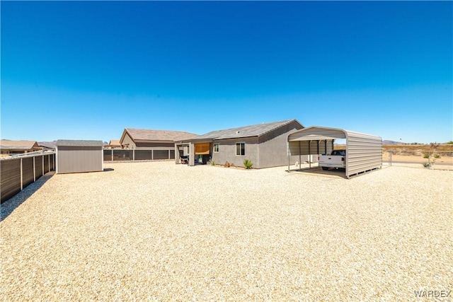 rear view of property featuring fence, an outdoor structure, a detached carport, and a storage unit