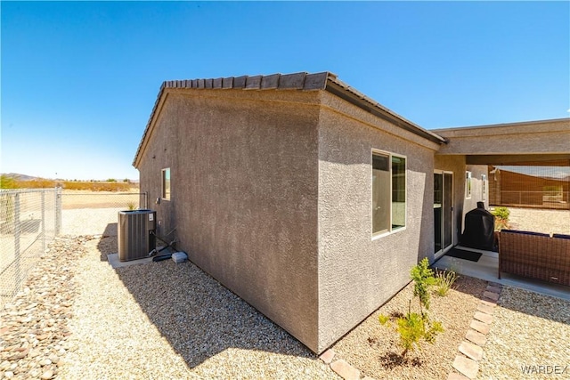 view of side of home featuring fence, stucco siding, and cooling unit