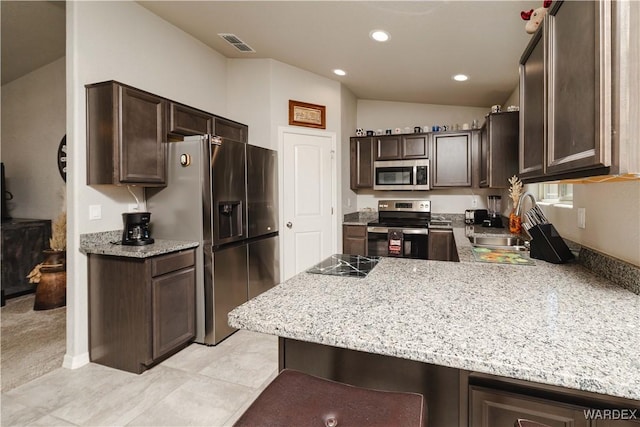 kitchen with stainless steel appliances, dark brown cabinetry, a sink, and a peninsula