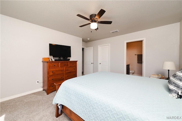 bedroom featuring ceiling fan, visible vents, light colored carpet, baseboards, and ensuite bath