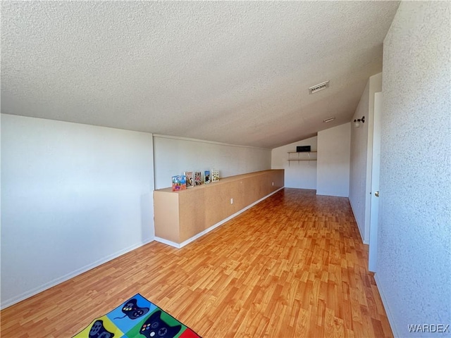 additional living space featuring lofted ceiling, visible vents, a textured ceiling, and light wood finished floors