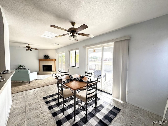 dining room with ceiling fan, a textured ceiling, and a tile fireplace