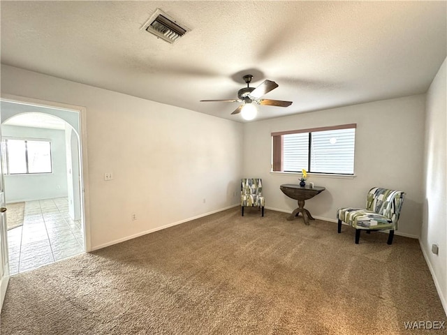 unfurnished room with visible vents, arched walkways, a ceiling fan, a textured ceiling, and carpet flooring