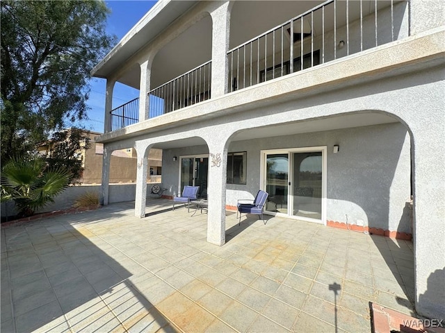 rear view of property featuring a balcony, a patio, and stucco siding