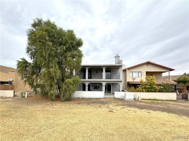 back of property featuring a balcony, a chimney, fence, a yard, and stucco siding