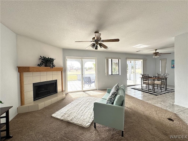 living room with carpet floors, ceiling fan, a textured ceiling, a tile fireplace, and tile patterned floors