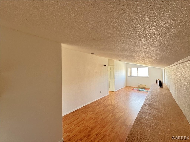 unfurnished room with a textured ceiling, baseboards, vaulted ceiling, and wood finished floors