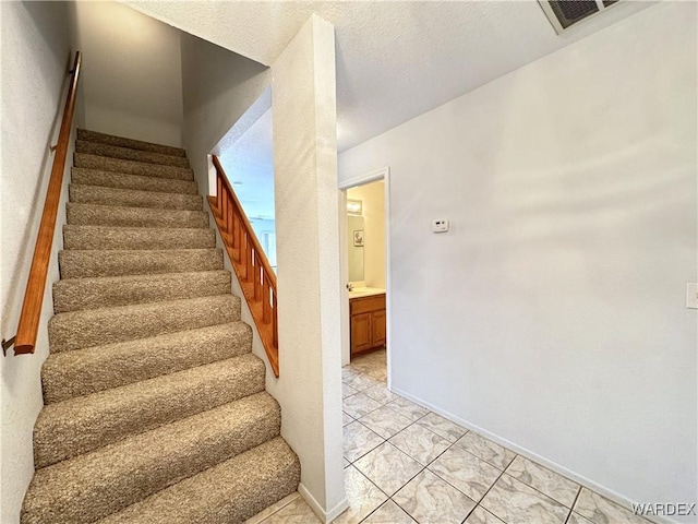 stairway featuring visible vents, a textured ceiling, and baseboards