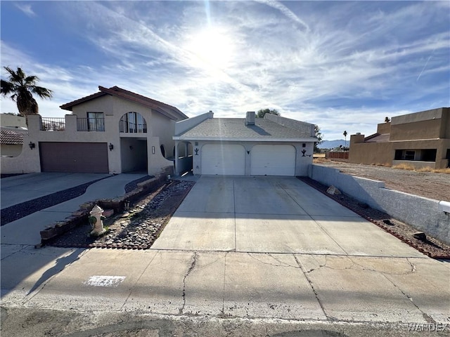 view of front of property with a garage, concrete driveway, a balcony, fence, and stucco siding