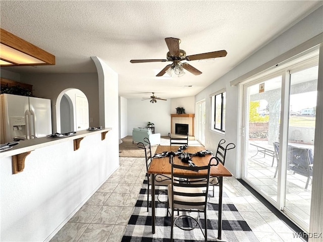 dining space featuring a ceiling fan, a fireplace with raised hearth, and a textured ceiling