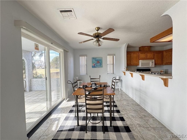 dining area featuring light tile patterned floors, visible vents, baseboards, a ceiling fan, and a textured ceiling