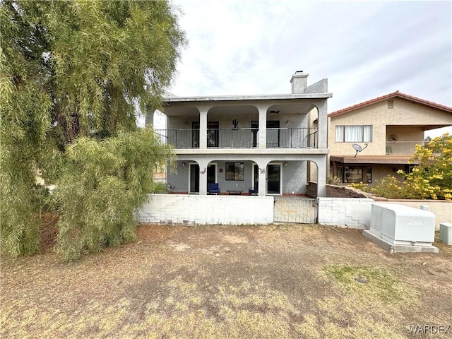 back of house featuring a balcony, a chimney, and stucco siding