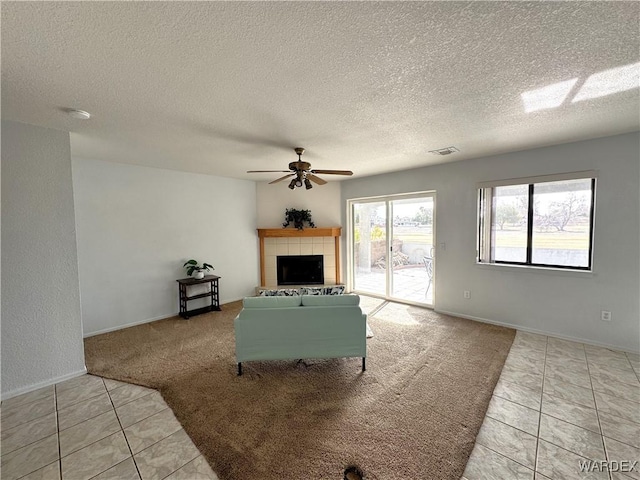 unfurnished living room featuring visible vents, a ceiling fan, a tiled fireplace, light colored carpet, and light tile patterned flooring