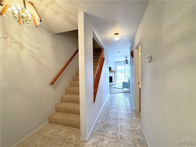 hallway featuring a textured ceiling, a textured wall, stairway, and baseboards