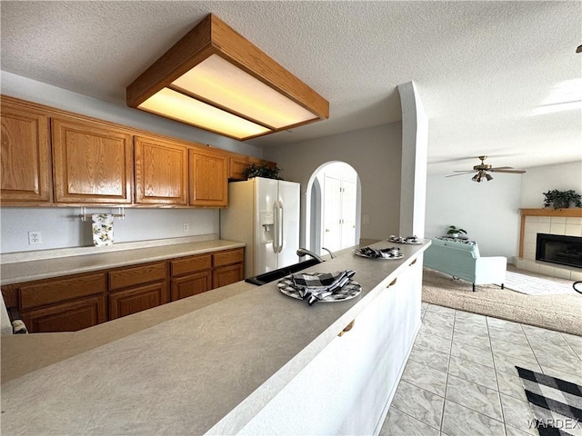 kitchen with light countertops, brown cabinetry, open floor plan, a sink, and white fridge with ice dispenser