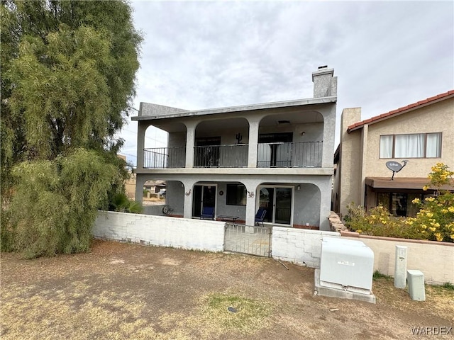 back of property with a chimney, a fenced front yard, a balcony, and stucco siding