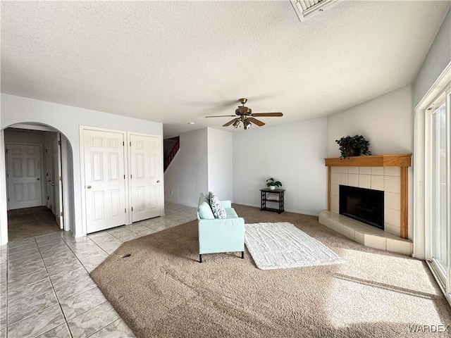 unfurnished living room featuring arched walkways, ceiling fan, a textured ceiling, and a tiled fireplace